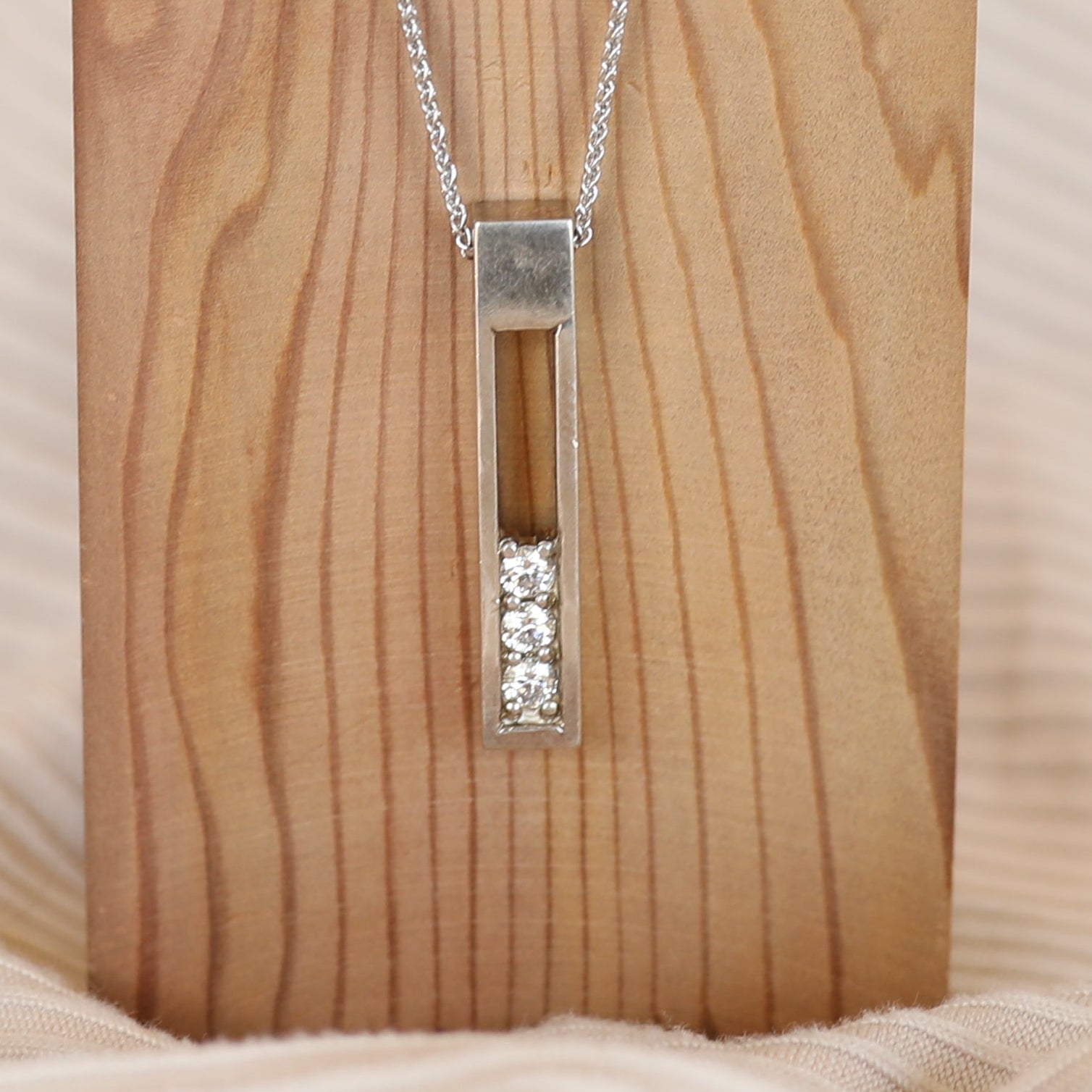 Silver necklace with a rectangular pendant on a wooden stand against a beige fabric background