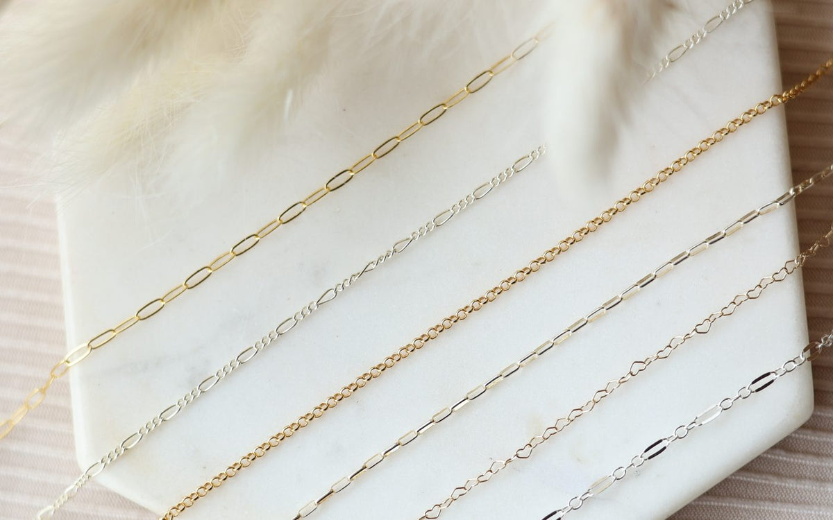 Fine gold and silver permanent jewelry chains on marble